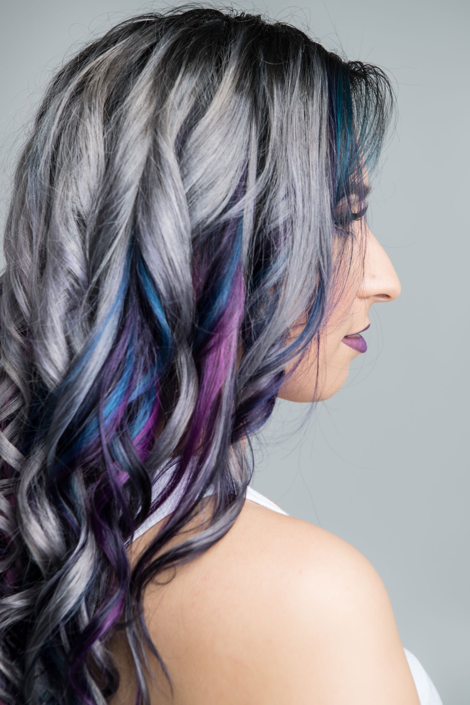 Side view of a long hair style. Hair is mostly silver with blue and purple streaks mixed at the ends.