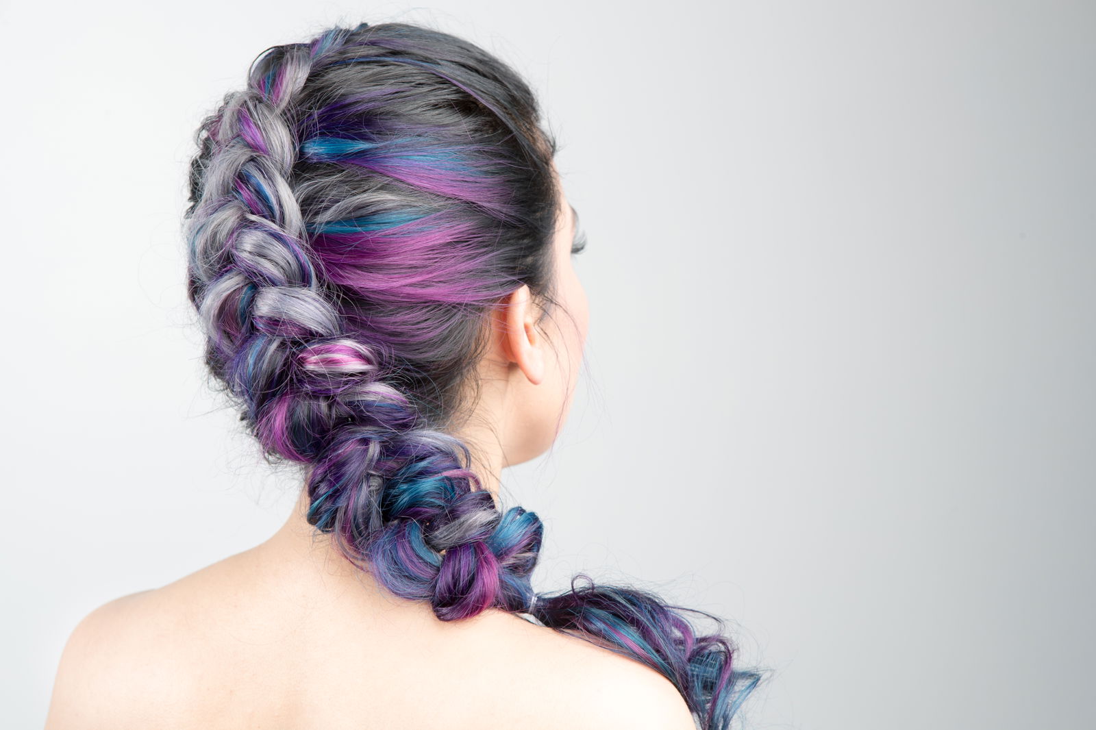 Back view of a long hair style swept up in a braid. Hair is mostly silver with blue and purple streaks mixed at the ends.