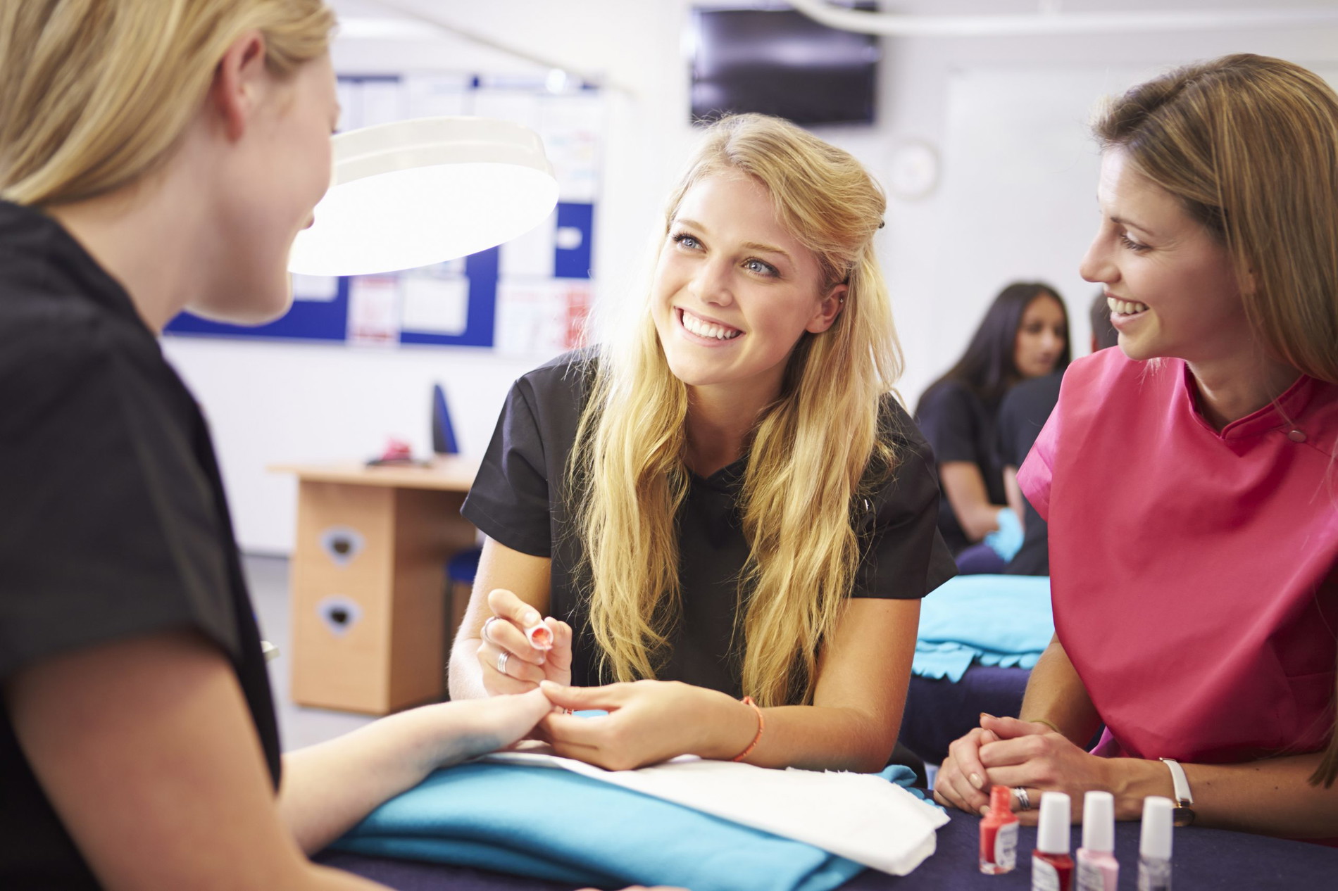 Teacher Helping Students Training To Become Beauticians Painting Nails Smiling